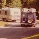 A van with two canoes strapped to the top follows another van pulling a camping trailer